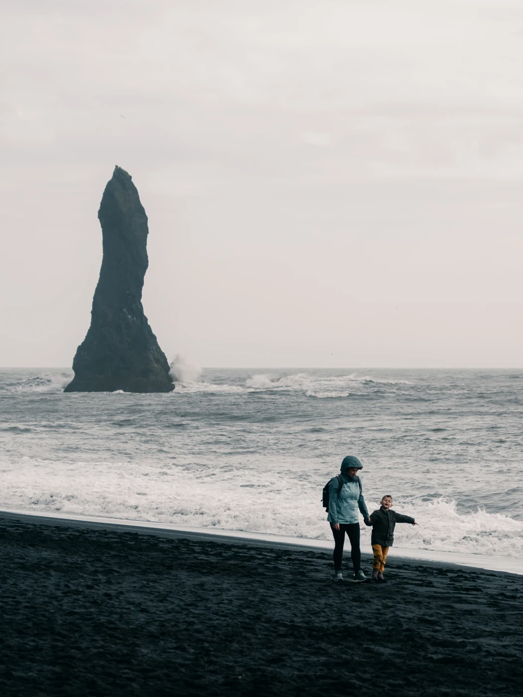 Viaggiatori davanti alle onde e a un faraglione islandese